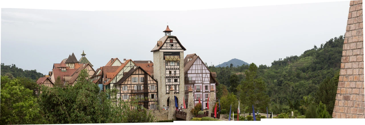 Tall houses with steep red roofs and exposed timber framing in front of a green hillside.