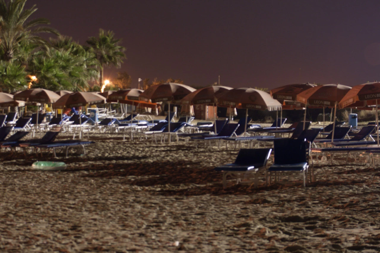 Empty sun loungers and parasols on a lit beach after dark.