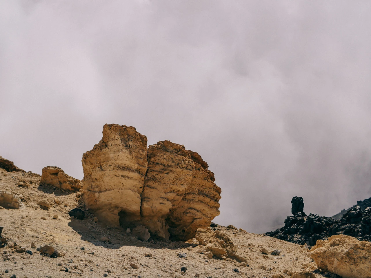 A warm brown rock formation stands in a mountain landscape surrounded by low cloud.