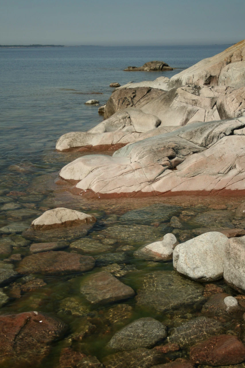 Stenar syns under genomskinligt grunt vatten vid en klippkant.