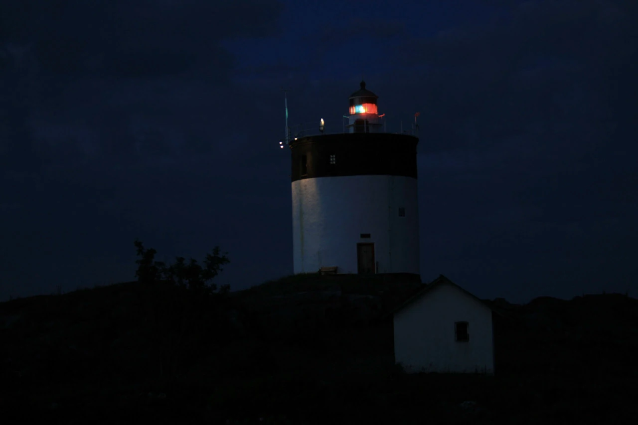 En ensam röd signal lyser från en vit fyr i mörkret.