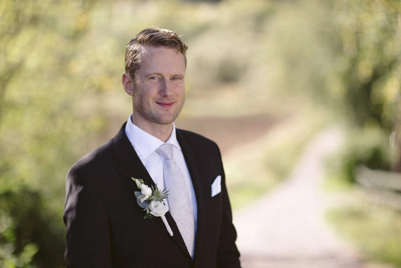 Porträtt av brudgummen i mjukt ljus mellan träden.