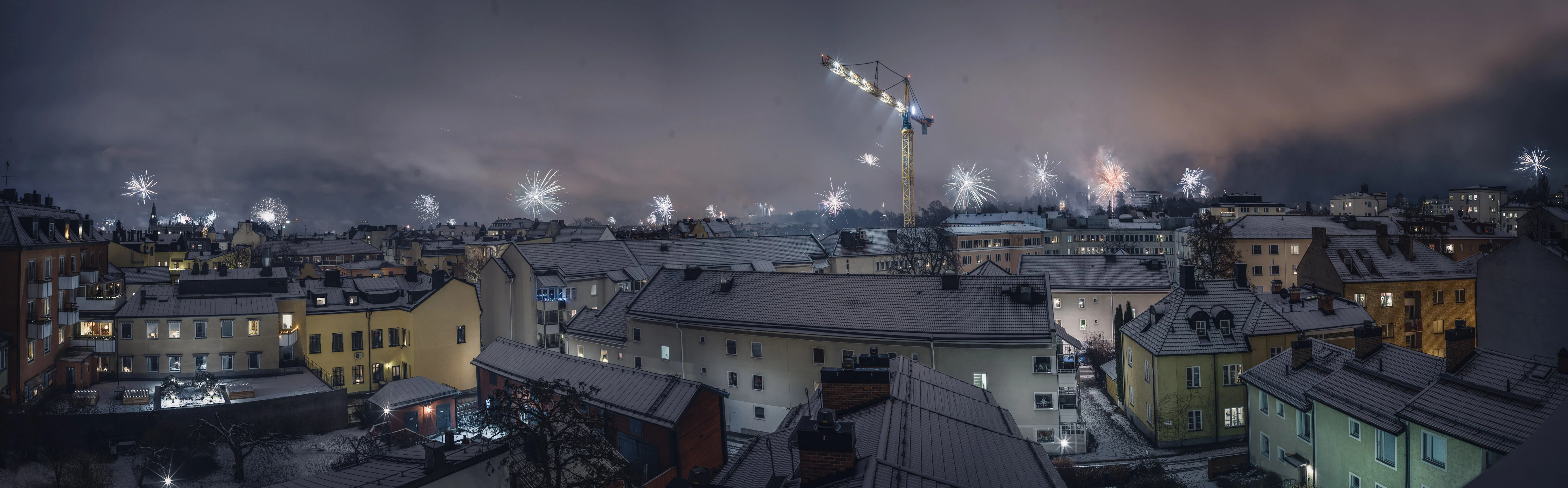 A wide view across city rooftops with fireworks and smoke in the night sky.