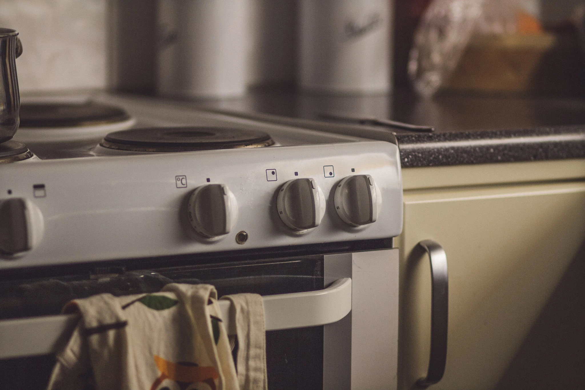 Close view of an old white electric cooker with round knobs and a towel on the oven door.