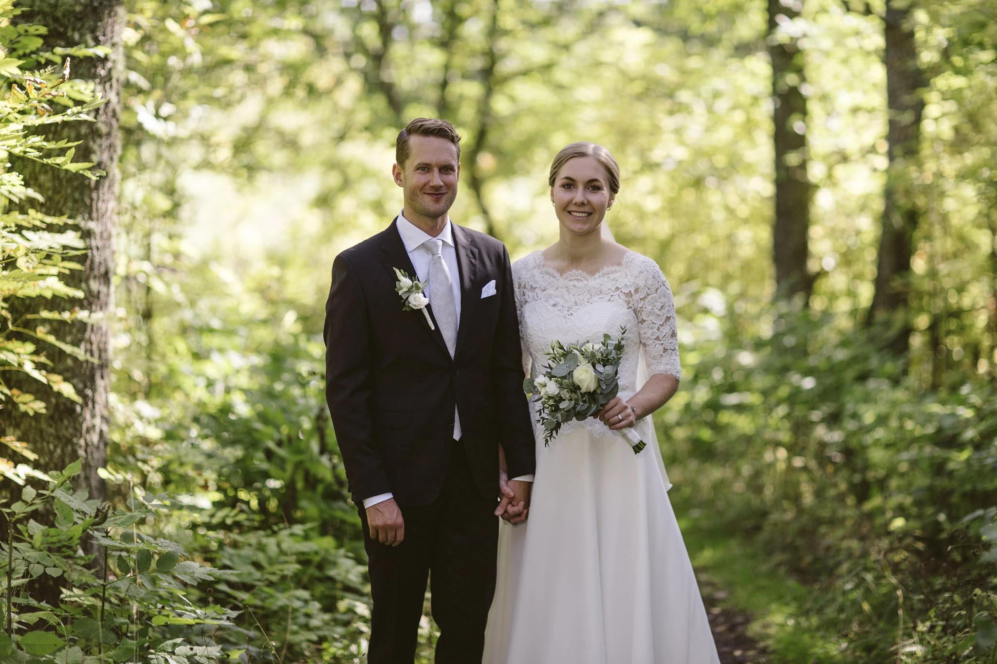 Brudpar står tillsammans i skogen, vända mot kameran.