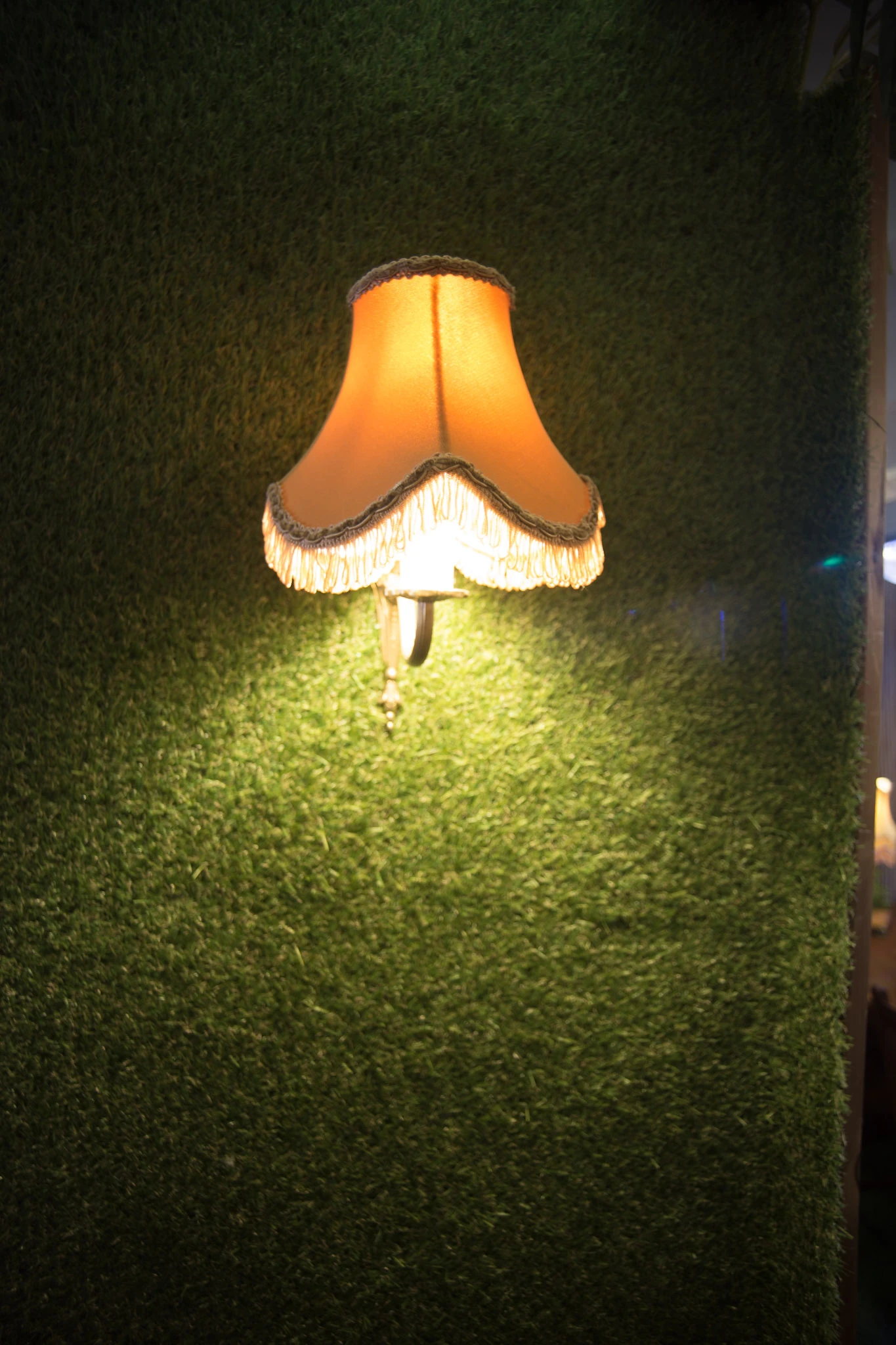 A small wall lamp with a warm fabric shade glows against a dark green wall.