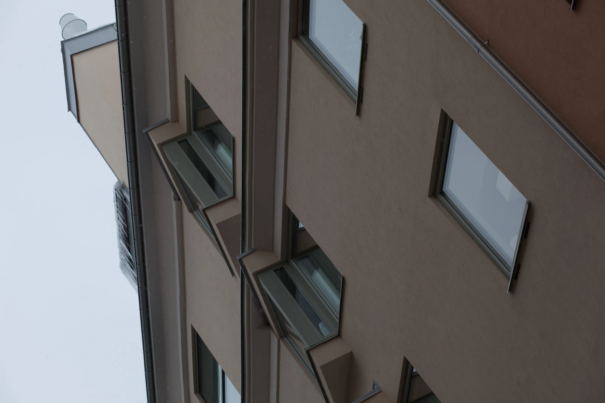 Two angular projecting windows extend from a brown plaster facade seen diagonally from below.