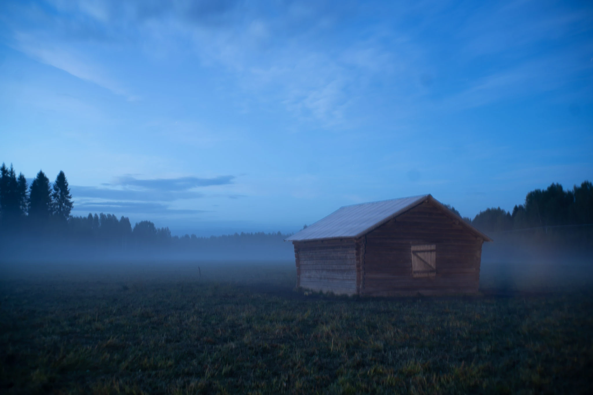 A solitary wooden shed stands in a dark field in blue mist.