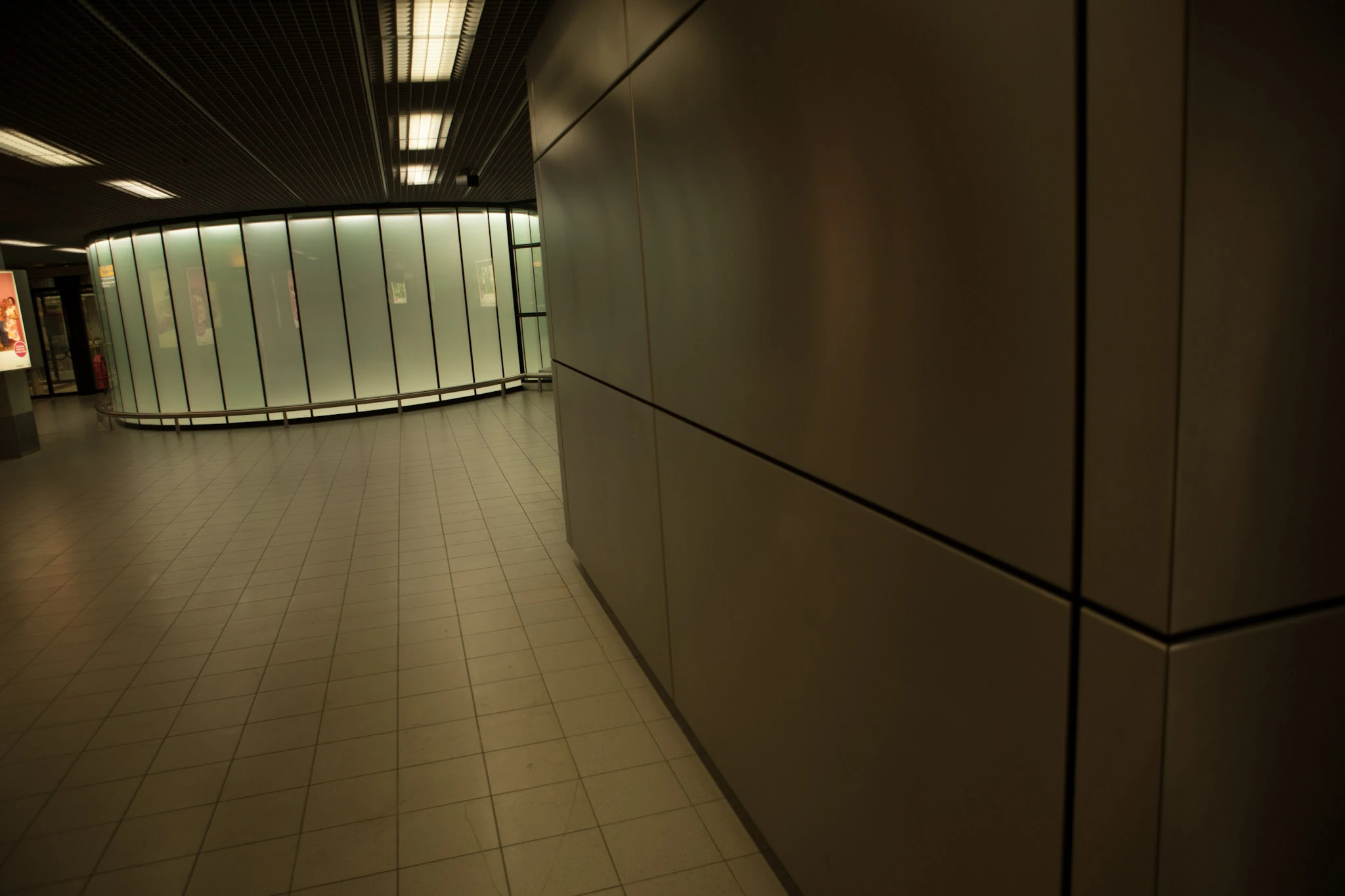 Kaklat golv och metallväggar möts i en tom passage under lysrör.