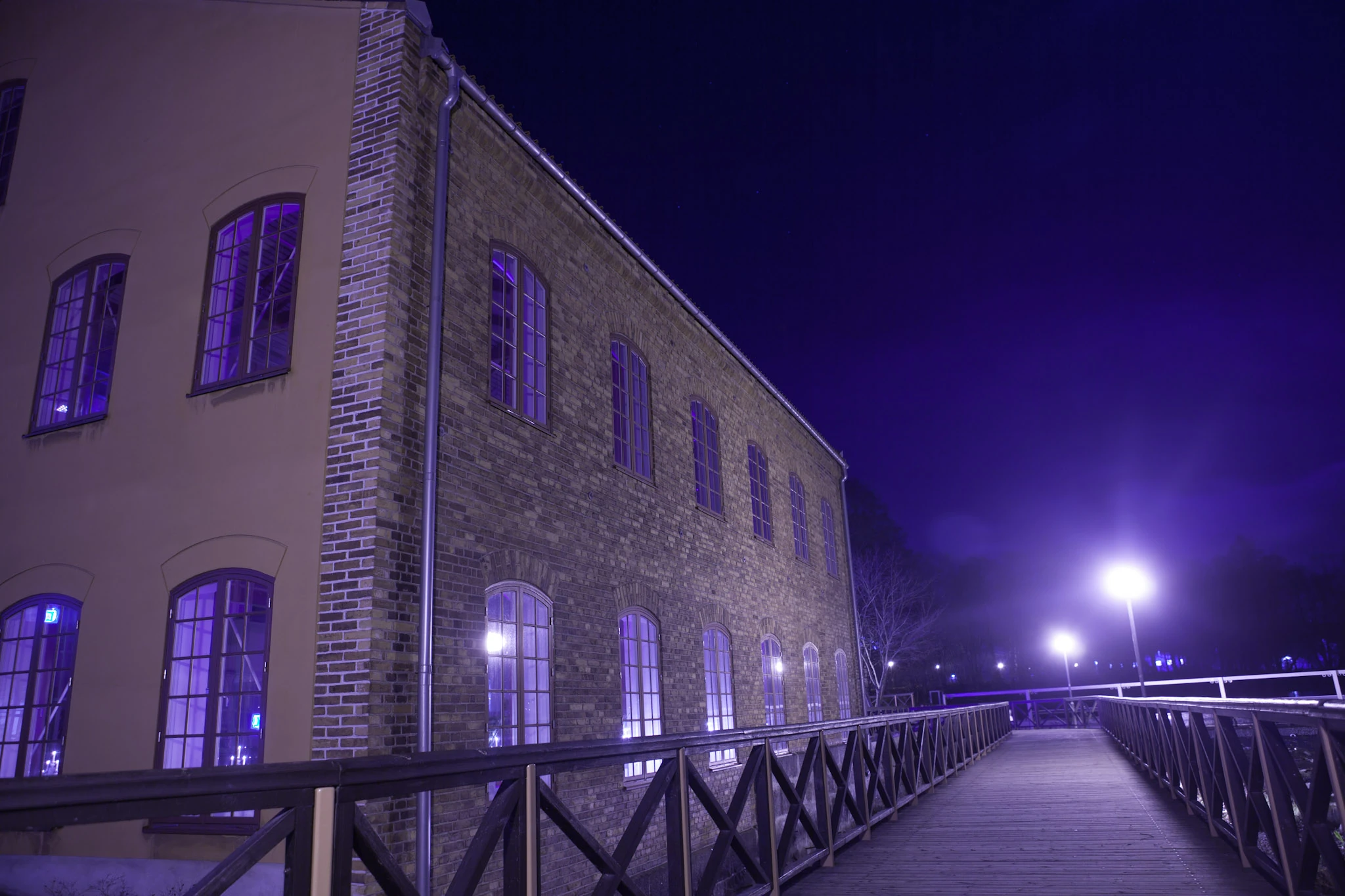 An old brick building and a railing lit by purple light against a dark sky.