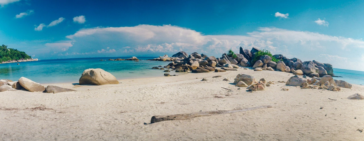 Ljus sand och låga klippor under en stor blå himmel.