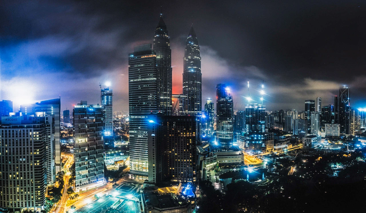 A dense skyline of illuminated towers beneath dark blue clouds.