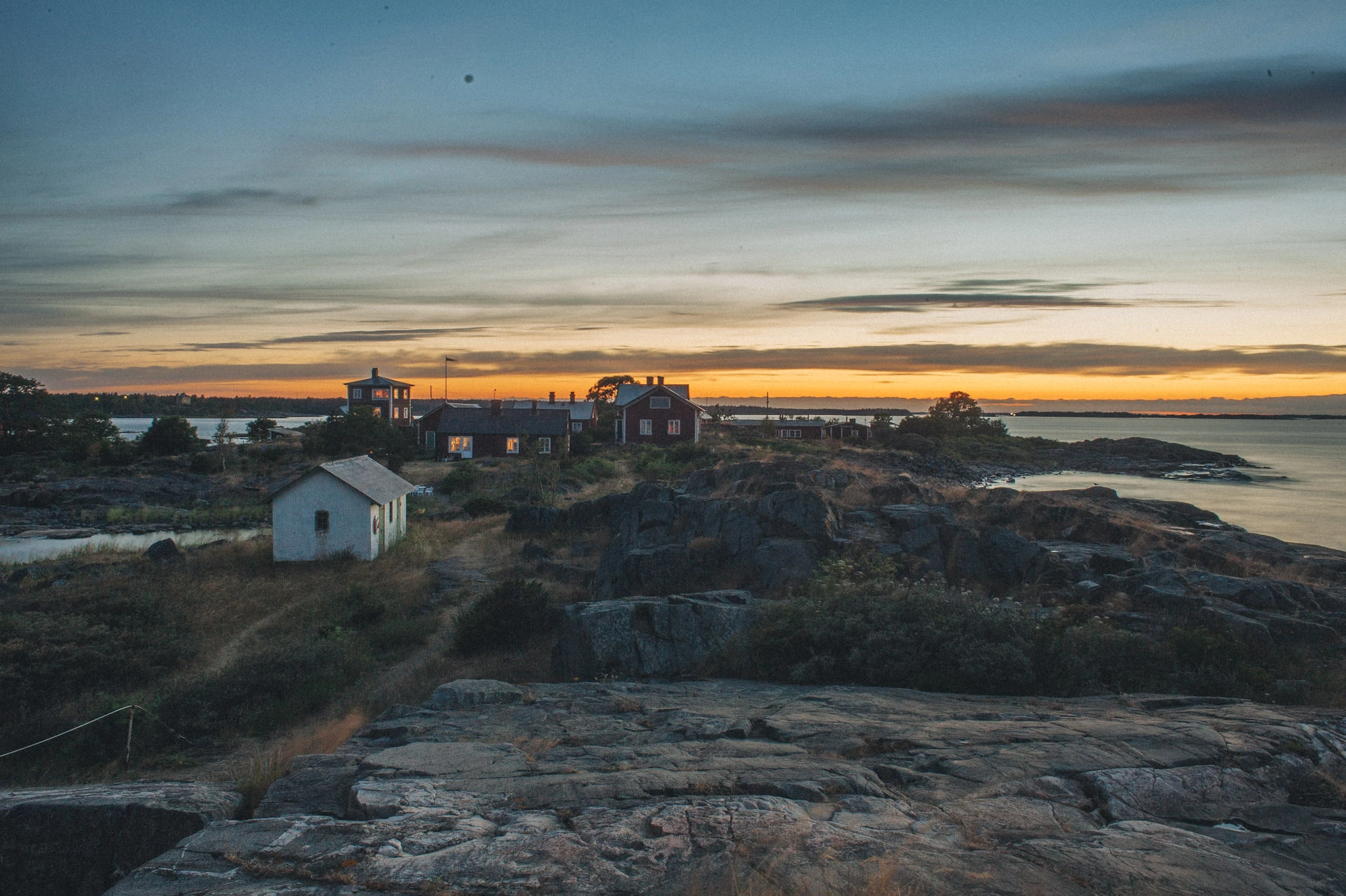 Small houses and rocks in an archipelago beneath a narrow orange horizon.