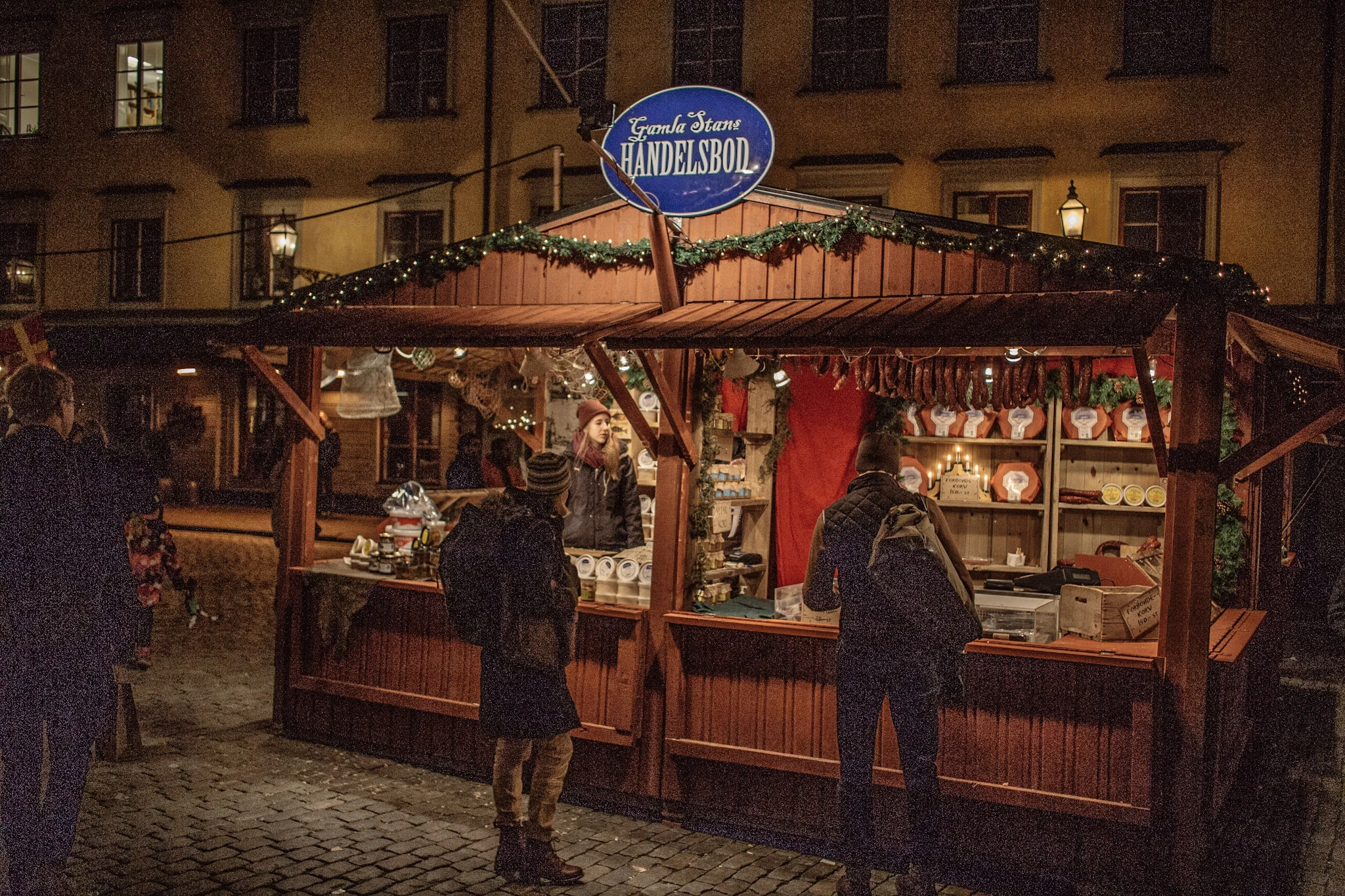 A red wooden market stall with Christmas decorations and visitors at night.
