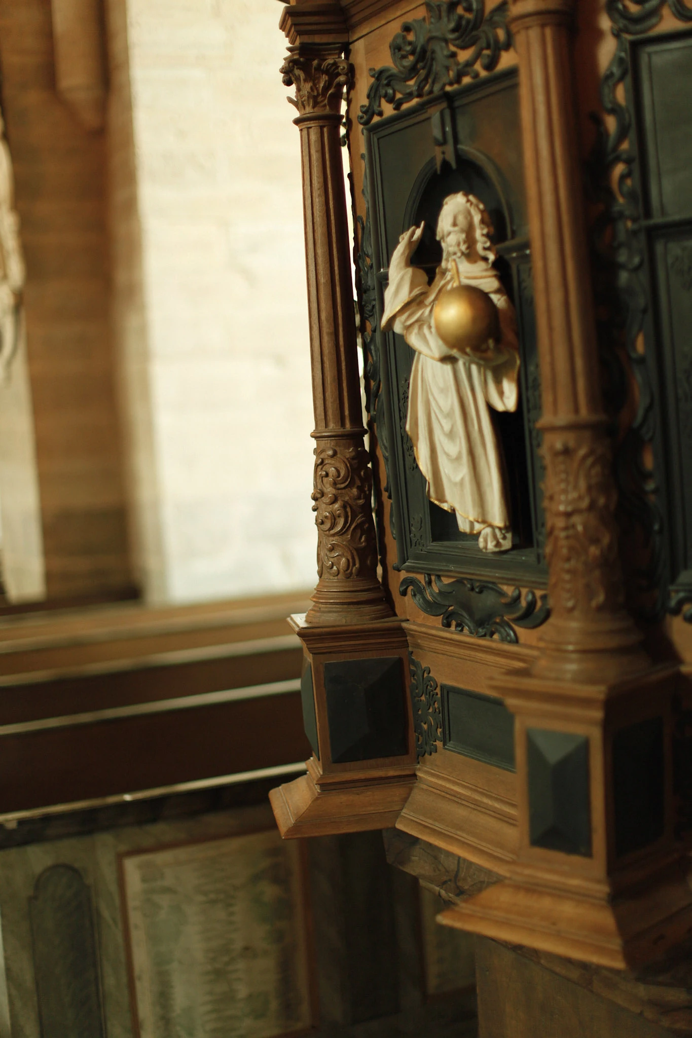A carved figure in an ornate wooden cabinet beside a pale stone column.