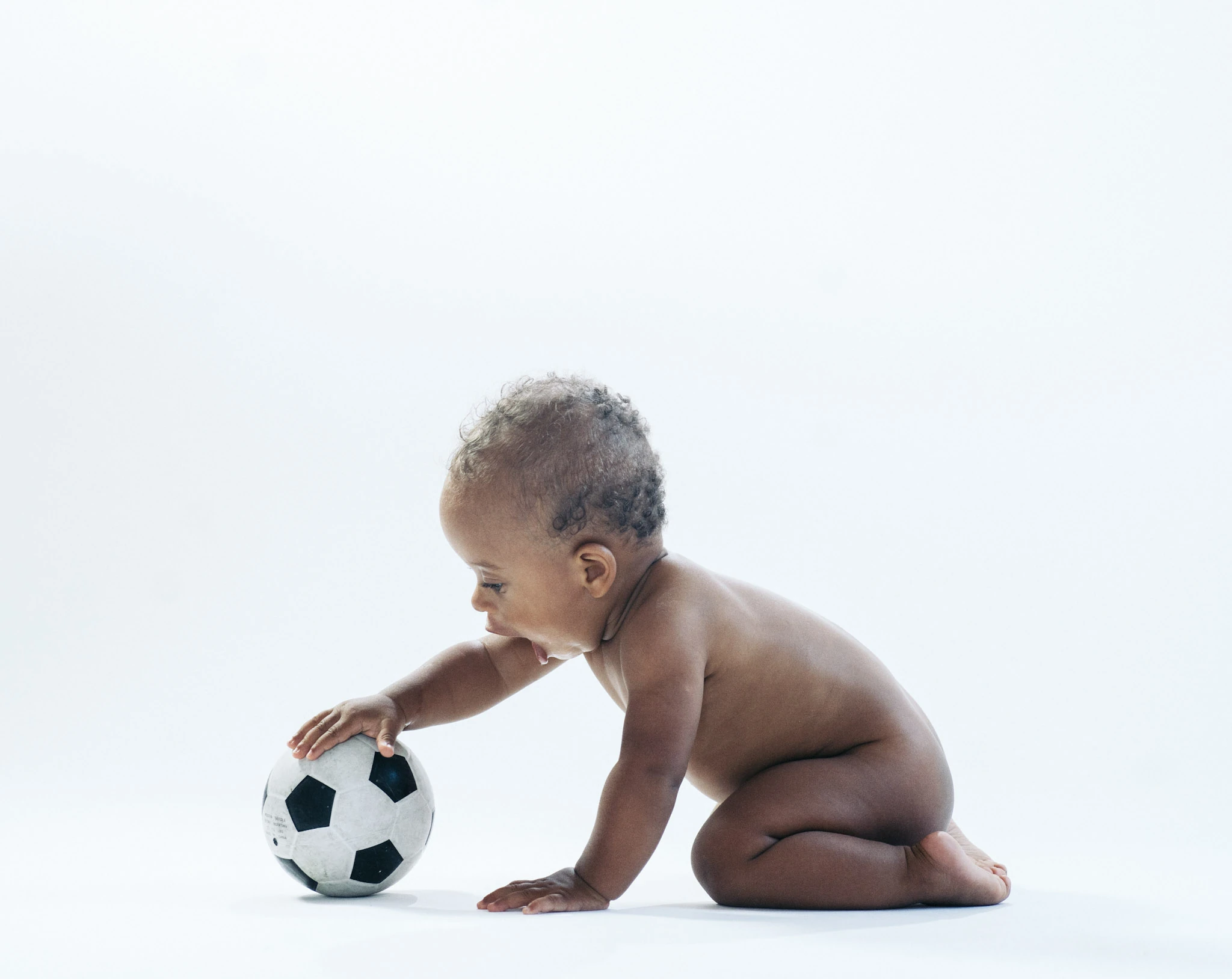 Ett litet barn leker med en fotboll mot vit bakgrund.