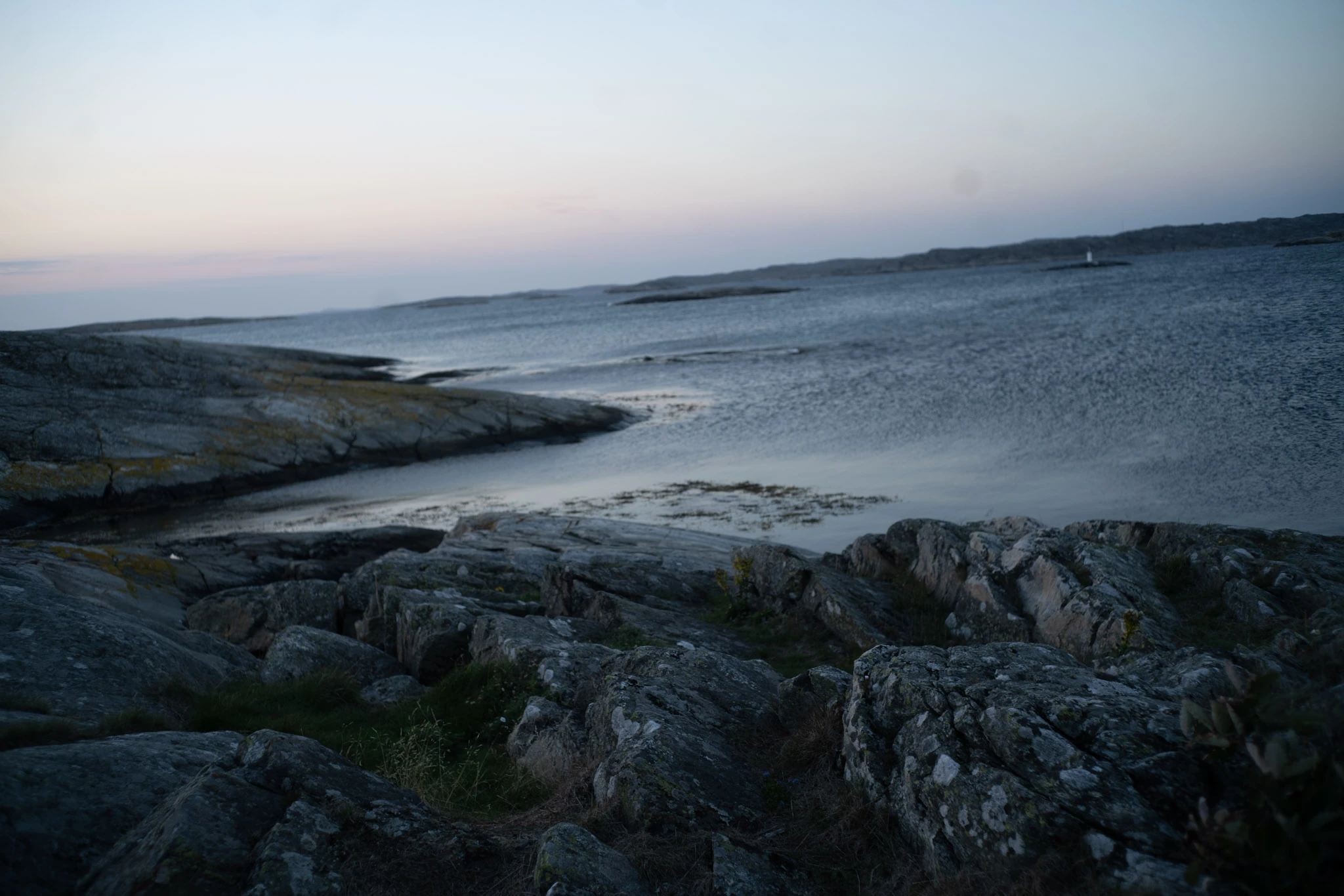 Dark rock slabs and still water beneath a pale pink evening sky.