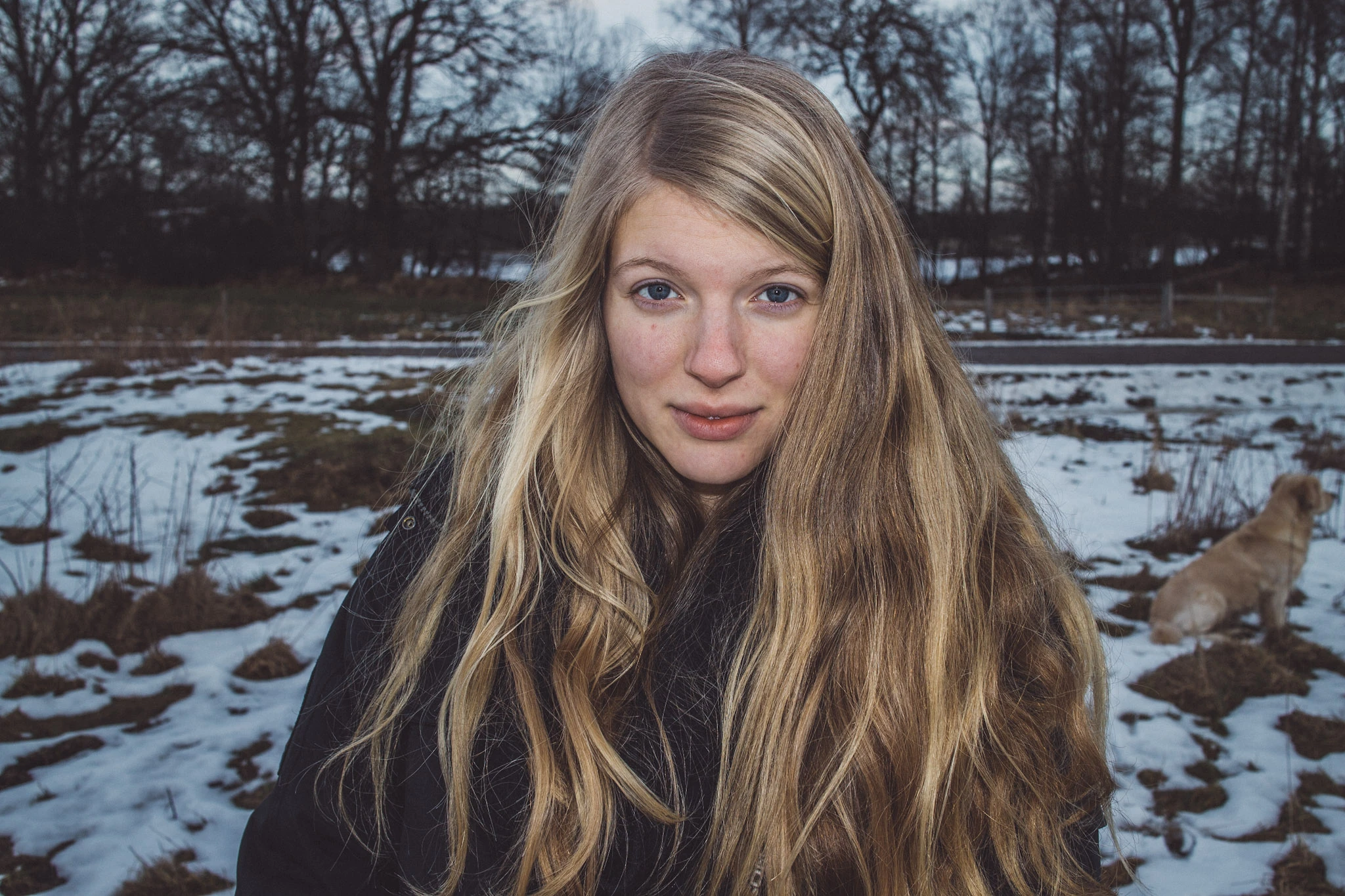 En blond kvinna i mörk jacka framför ett snötäckt fält.
