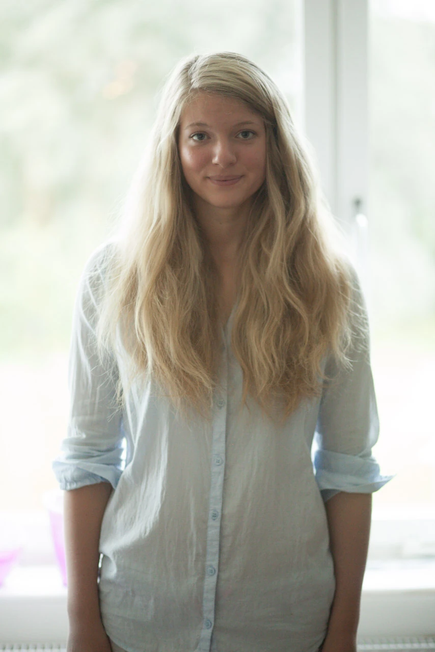 En blond kvinna står framför ett ljust fönster i mjuka vita toner.