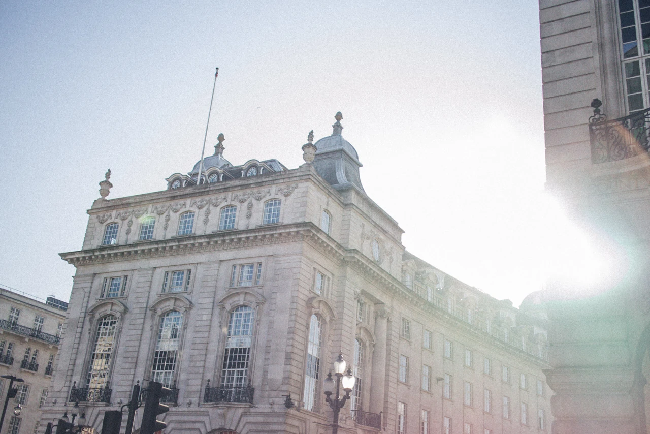The sun breaks out behind a large stone building in a city.