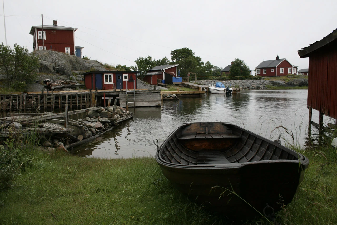 En mörk träbåt ligger i gräset vid en liten hamn.