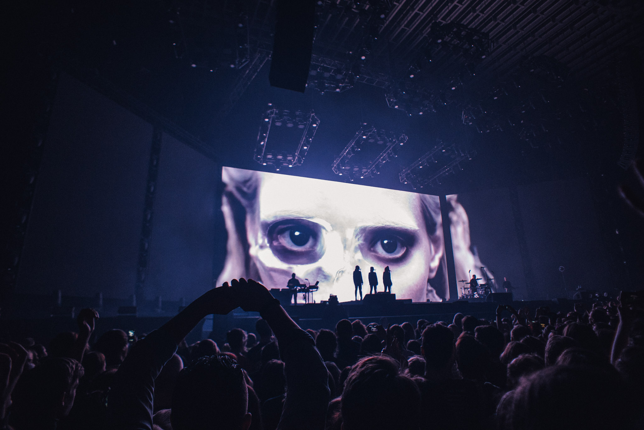A large face projection behind a band, with the audience silhouetted in the foreground.