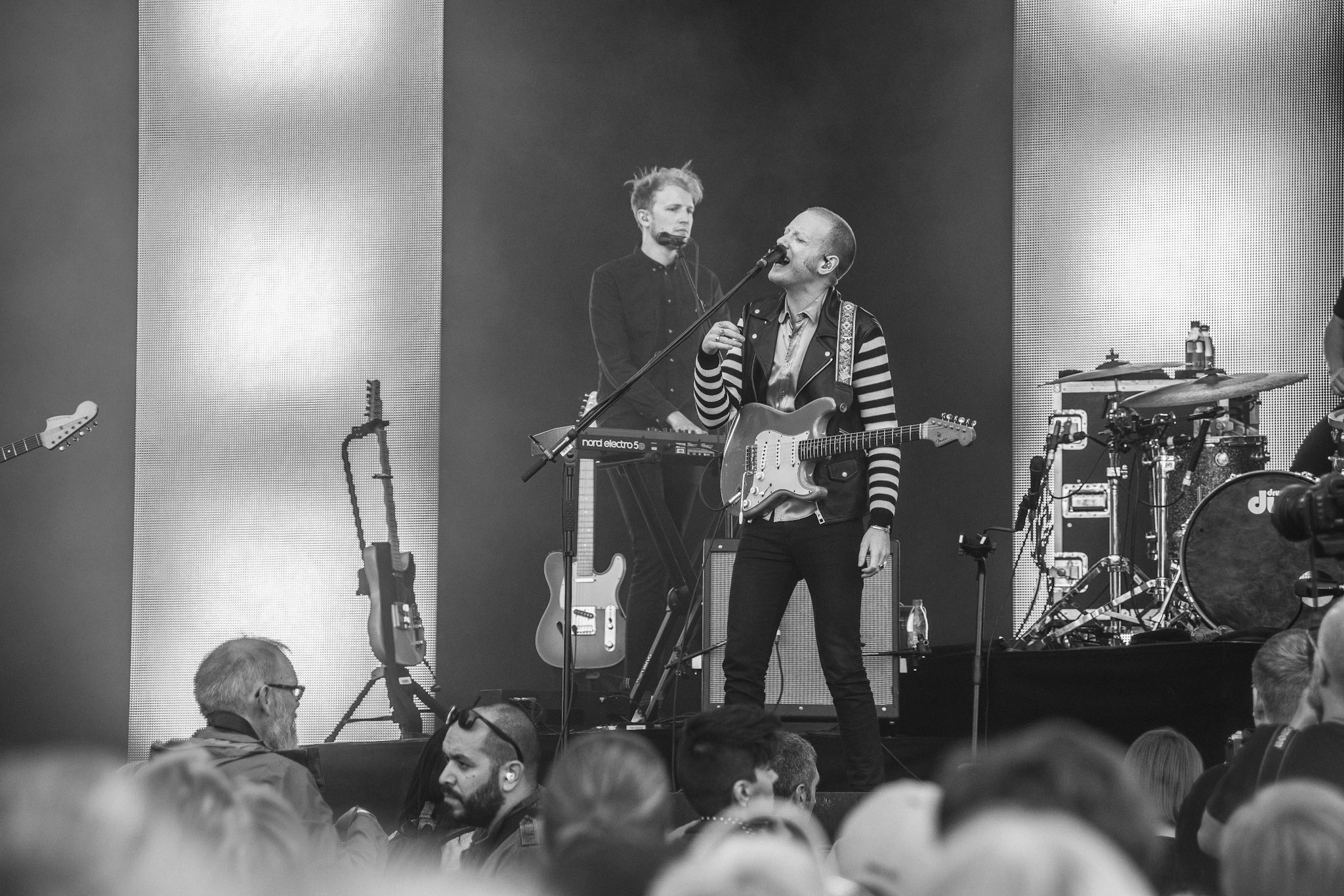 Två musiker möts vid en mikrofon på en scen, fotograferade i svartvitt.
