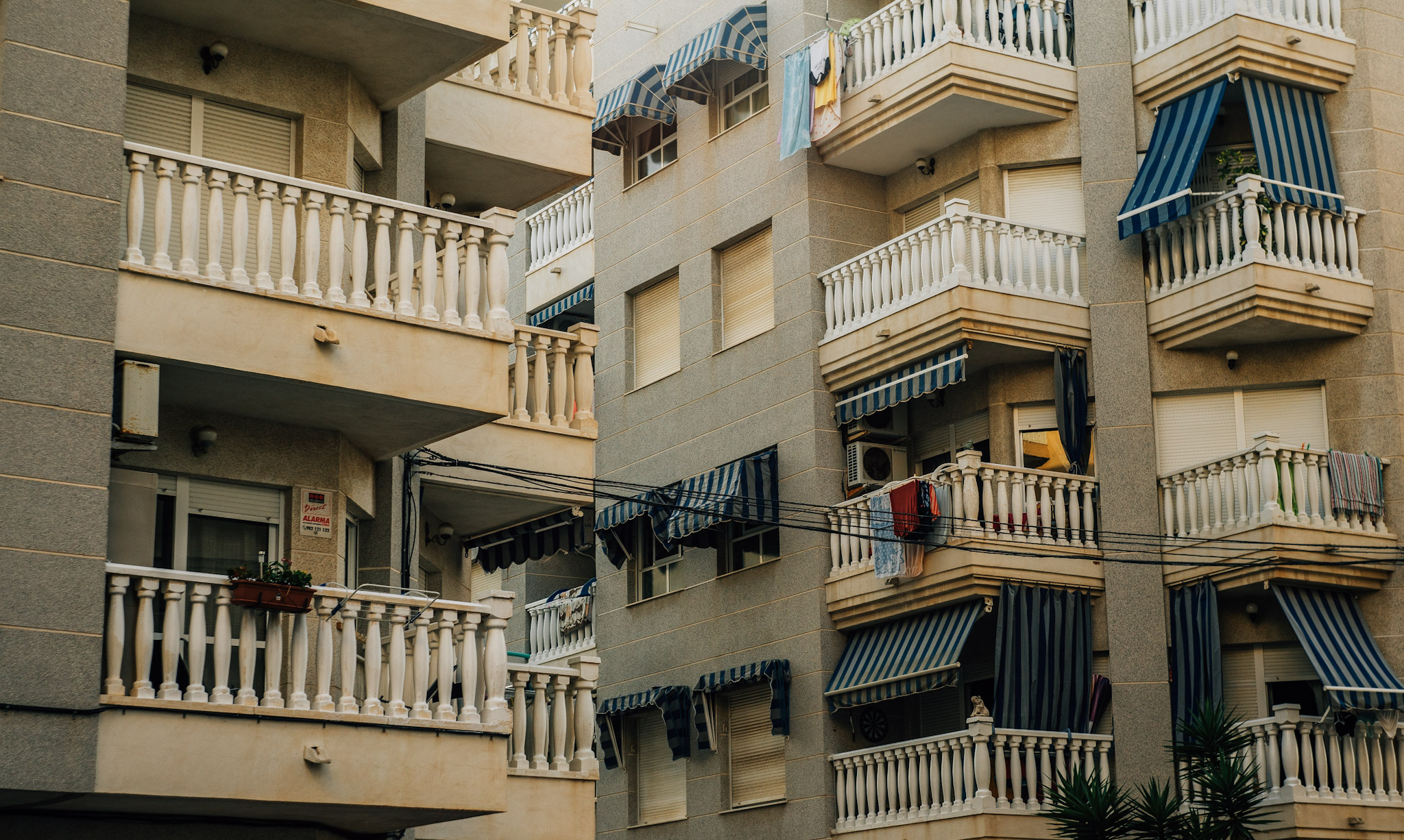Balconies with white railings, striped awnings and hanging laundry on a warm-toned facade.